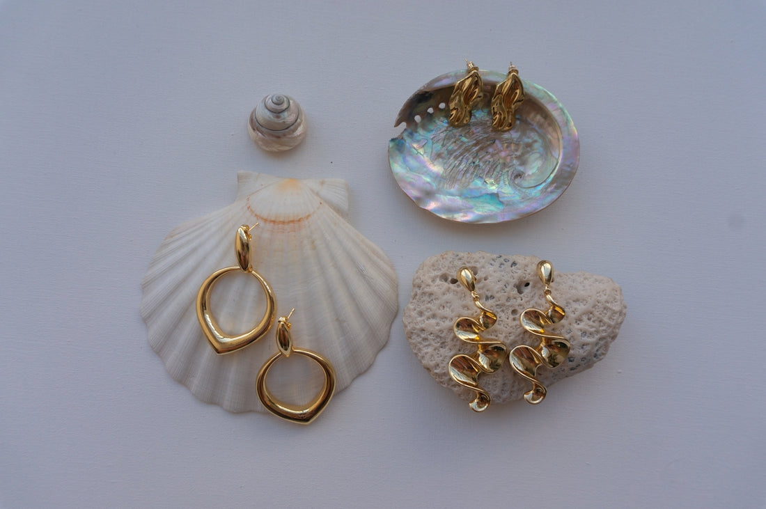 Gold earrings displayed on seashells and coral.
