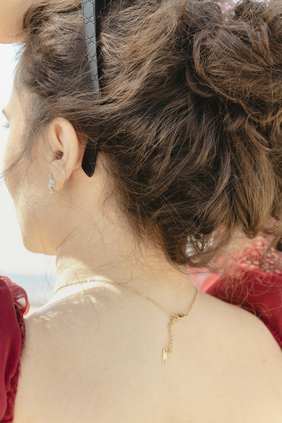 Woman's back with curly hair, sunglasses, and gold necklace.