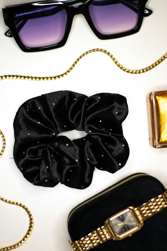 A black velvet scrunchie with rhinestones, sunglasses, a gold chain, and a watch